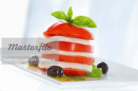 A tomato and mozzarella tower with basil and olives A tomato and mozzarella tower with basil and olives