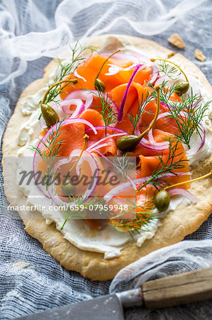 A blind-baked pizza base topped with cream cheese, smoked alpine salmon, dill, red onions and capers