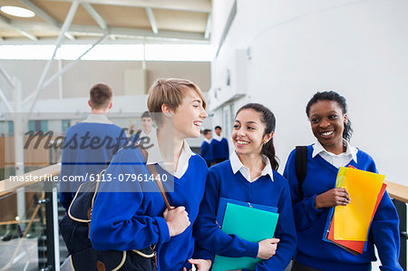 Smiling female students wearing school uniforms walking through school corridor