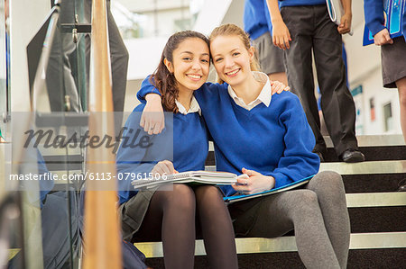 Portrait of two cheerful female students sitting on steps with arms around