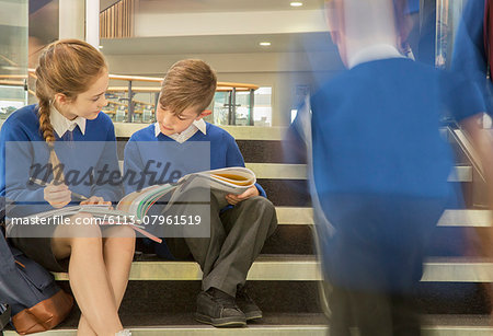 Elementary school children wearing school uniforms sitting on steps and writing in textbooks