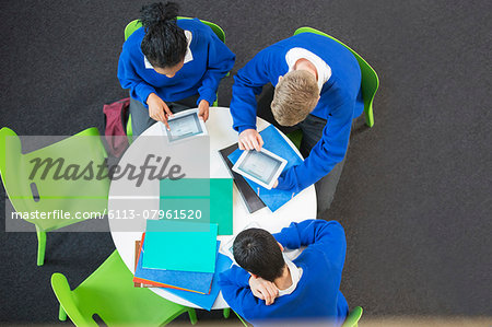 Overhead view of three students with digital tablets at round table