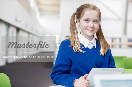 Portrait of smiling elementary school girl with blond pigtails holding digital tablet