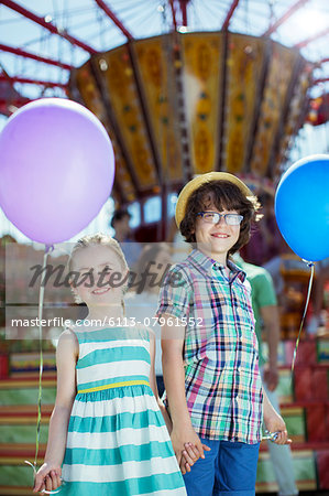 Portrait of boy and girl holding balloons in amusement park