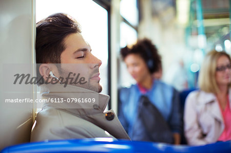 Businessman napping and listening to earbuds on train Businessman napping and listening to earbuds on train