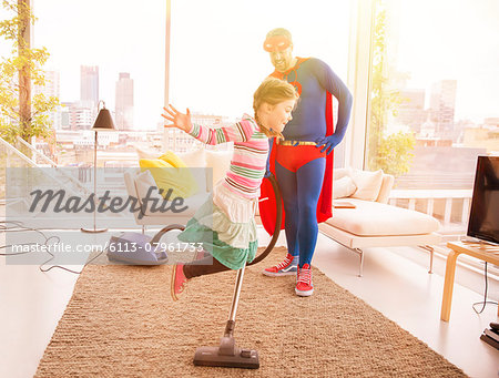 Superhero father vacuuming while daughter jumps in living room