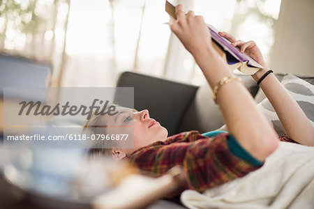 Young woman lying on a sofa, reading a book.