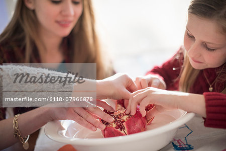 Two girls and a woman sitting at a table, picking kernels from a pomegranate.