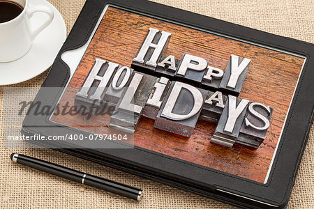 Happy Holidays greetings  in vintage metal type printing blocks on a digital tablet with a cup of coffee