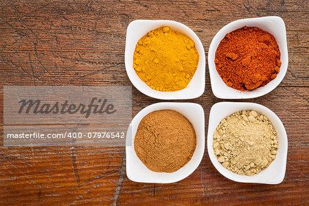 four healthy spices (turmeric, ginger, cinnamon and paprika) in white bowls on a grunge wood