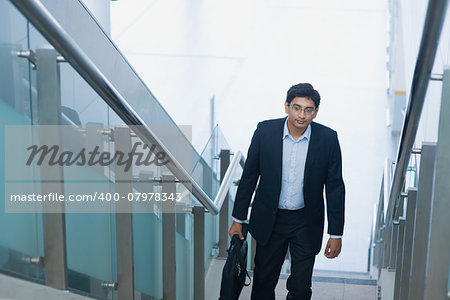 Asian Indian corporate businessman in suit with briefcase ascending steps.