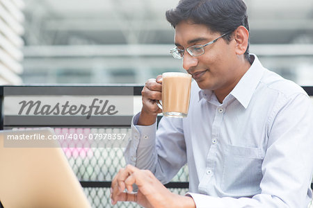 Asian Indian businessman using laptop computer while drinking a cup hot milk tea.