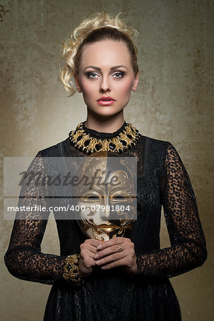 charming blonde girl posing in carnival shoot with antique baroque gothic costume, black lace dress, precious jewellery and theatrical mask in the hands