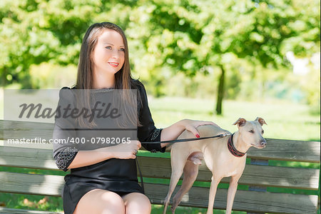 Young attractive girl sitting on bench with greyhound  in the park