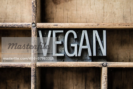 The word "VEGAN" written in vintage metal letterpress type sitting in a wooden drawer.