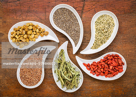 superfood samples  (mulberry, chia seeds, hemp seeds, goji berry, stevia leaf, flax seed) in teardrop shaped bowls against grunge wood