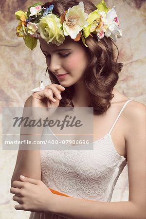 Beautiful, brunette woman with colorful makeup, wreath of flowers on head, little bird on her finger and wearing white dress.
