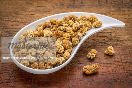 dried white mulberry on a teardrop shaped bowl against rustic wood