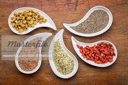 superfood samples  (mulberry, chia seeds, hemp seeds, goji berry, flax seed) in teardrop shaped bowls against grunge wood