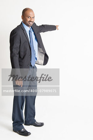 Full body Indian businessman pointing away to copy space, on plain background.