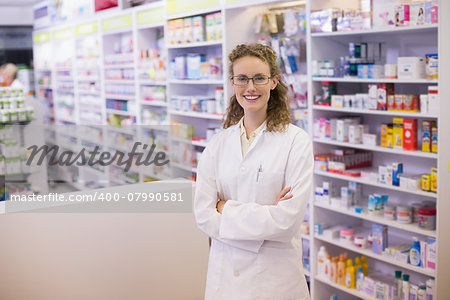 Portrait of a smiling pharmacist in lab coat with arms crossed in the pharmacy