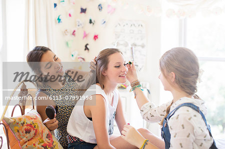 Three teenage girls doing make up and brushing hair in bedroom