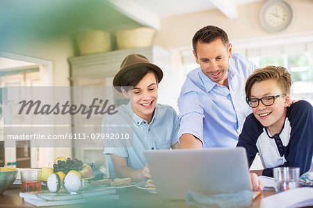 Mid adult man with teenage boys using laptop in kitchen