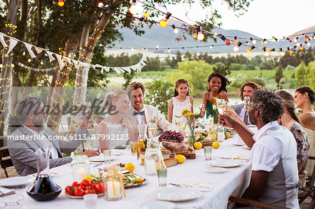 Young couple and their guests sitting at table during wedding reception in garden