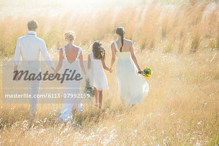 Young couple with bridesmaid and girl walking in meadow