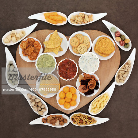 Savoury snack and dip party food selection in porcelain dishes  on a heart shaped wooden board.