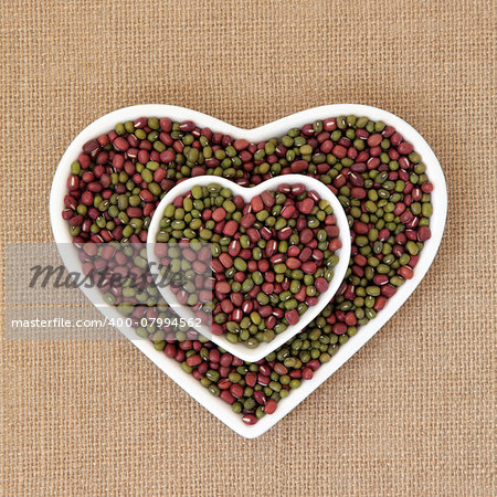 Mung and aduki beans in a heart shaped bowl over hessian background.