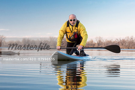 Senior male on stand up paddling (SUP) board. Early spring on calm lake in Colorado.