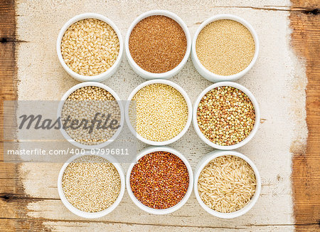 healthy, gluten free grains abstract (quinoa, brown rice, millet, amaranth, teff, buckwheat, sorghum), top view of small round bowls against rustic barn wood