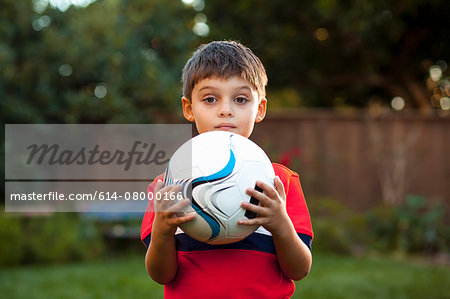 Boy holding football against chest in garden