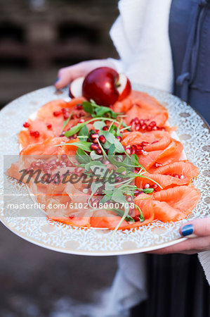 Person holding tray with smoked salmon and pomegranate seeds