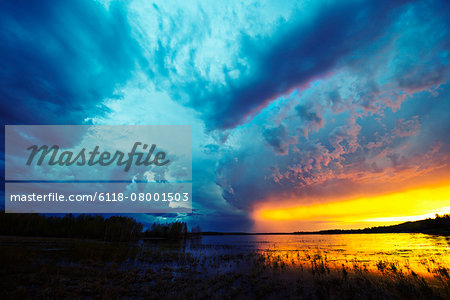 Sunset on the horizon over a lake, and storm clouds rising.