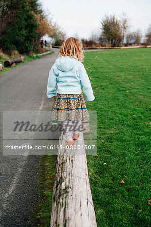 View from behind of a four year old girl walking and balancing on a log.