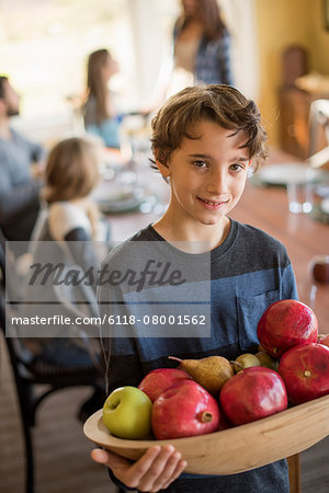 A boy carring a wooden tray of apples.