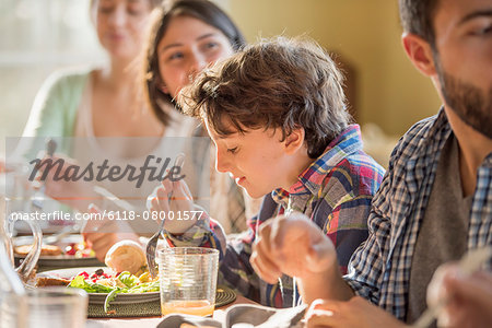 A group of people, adults and children, seated around a table for a meal. A group of people, adults and children, seated around a table for a meal.