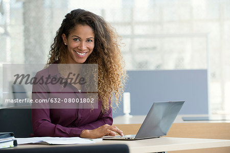 Businesswoman using laptop computer in office, smiling, portrait