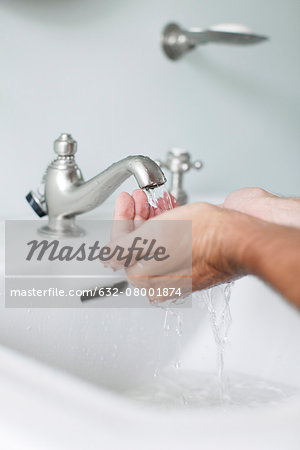 Man cupping hands beneath water running from bathroom faucet