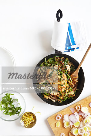 Skillet of Chicken, Arugula, Leeks, and Mushrooms with onions on cutting board, studio shot on white background