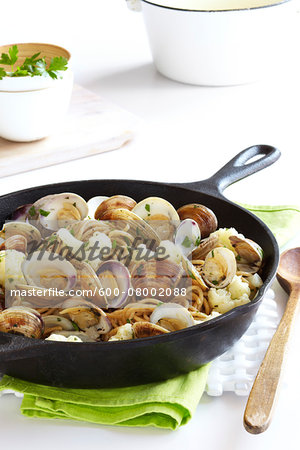 Cast iron skillet with whole wheat pasta, cauliflower and clams on a green napkin with a wooden spoon, studio shot
