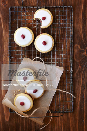 Sandwich cookies with icing and a cranberry on top, on a cooling rack, studio shot