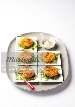 Individual potions of tuna cakes with arugul and dip on a platter, studio shot on white background