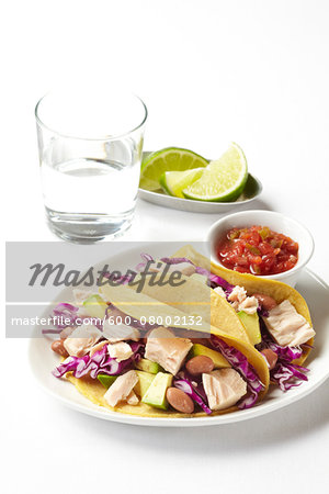 Tuna tacos with avocado, cabbage and beans on a white plate with salsa, limes and a glass of water, studio shot on white background Tuna tacos with avocado, cabbage and beans on a white plate with salsa, limes and a glass of water, studio shot on white background