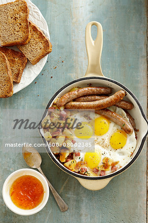 Overhead View of Skillet with Sunny Side up Eggs, Sausage, and Hashbrowns served with Whole Wheat Toast and Apricot Jam on Wooden Background
