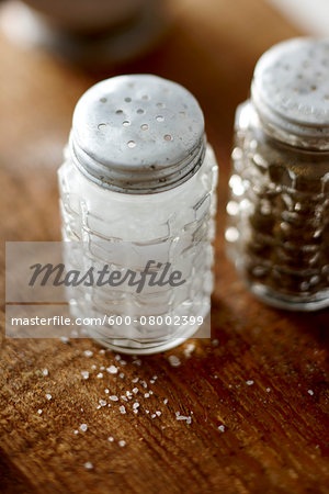 Vintage Cut Glass Salt and Pepper Shakers on Wooden Tabletop with Spilled Salt on Table Vintage Cut Glass Salt and Pepper Shakers on Wooden Tabletop with Spilled Salt on Table