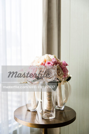 Bridal bouquets of pink and cream roses in vases on table by a window, Wedding Day preparations, Canada