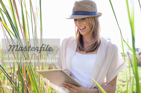 Mid adult woman sitting in long grass, using digital tablet
